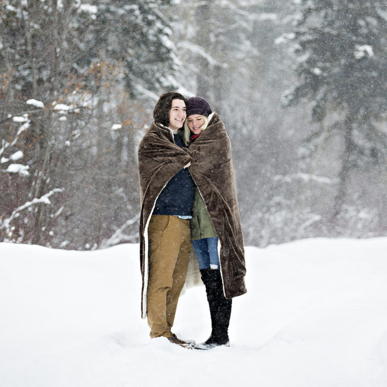 engagement photography of the bridge and groom to be bundled up in a blanket outside in a field