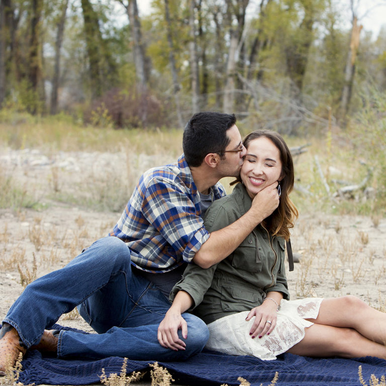 engagement photography of the bridge and groom to be bundled up in a blanket outside in a field