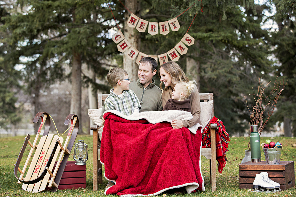 holiday portrait photography of a young brother and sister sitting outside on a bench with a holiday blanket and drinking hot chocolate out of Santa Claus mugs