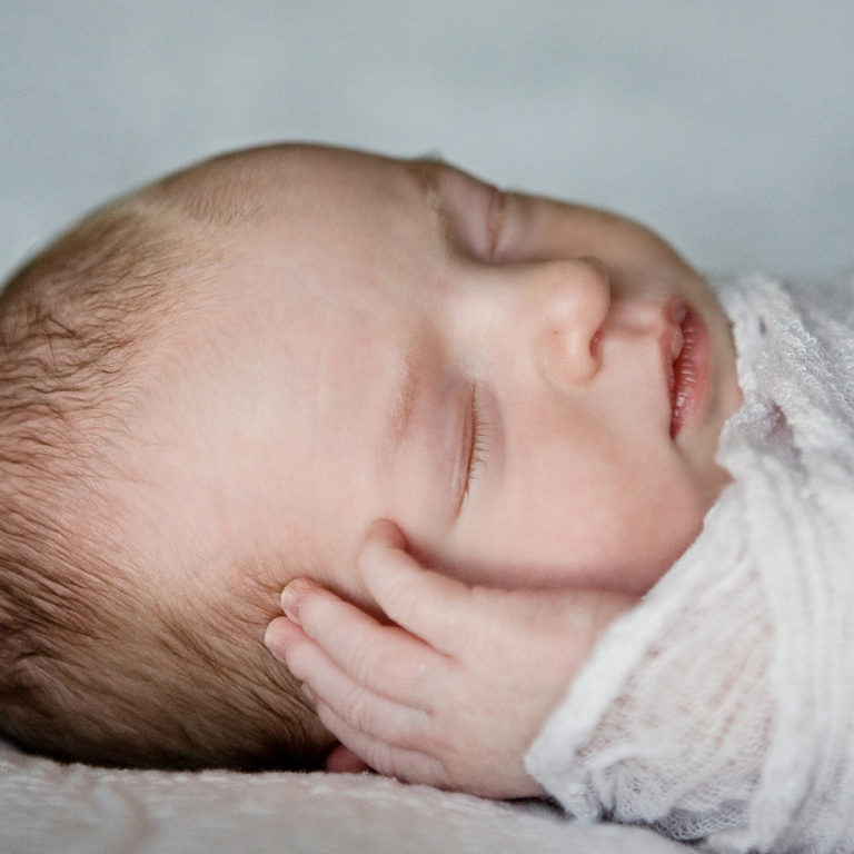 newborn photography of a newborn baby curled up sleeping on a white blanket