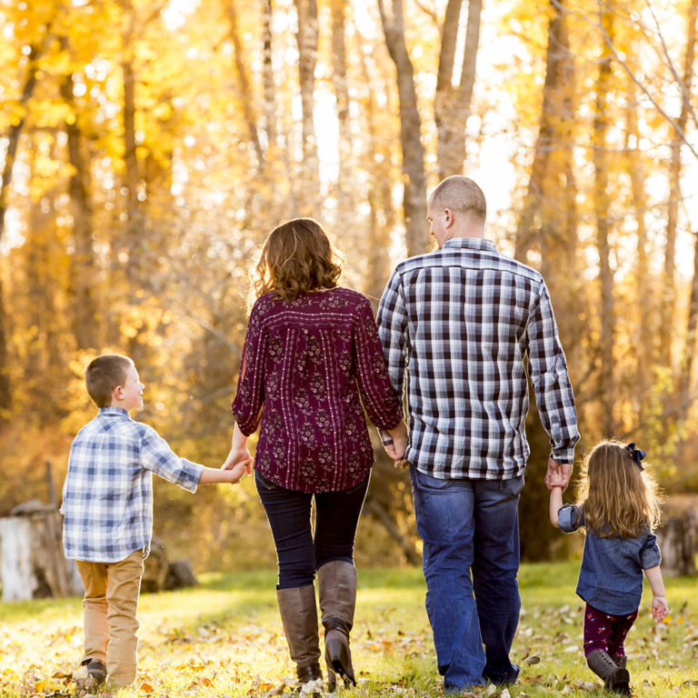 family portrait photography of a mother, father, and teenage daughter walking hand in hand through a field