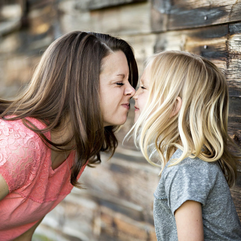 family portrait photography of three sisters standing in front of a brick wall and blowing flower petals out of their hands