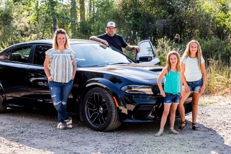 a man, woman and two pre-teen girls stand in front of car