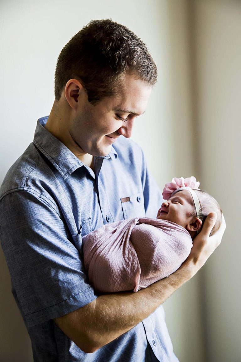 newborn photography of a new father smiling down at his newborn baby yawning in his arms