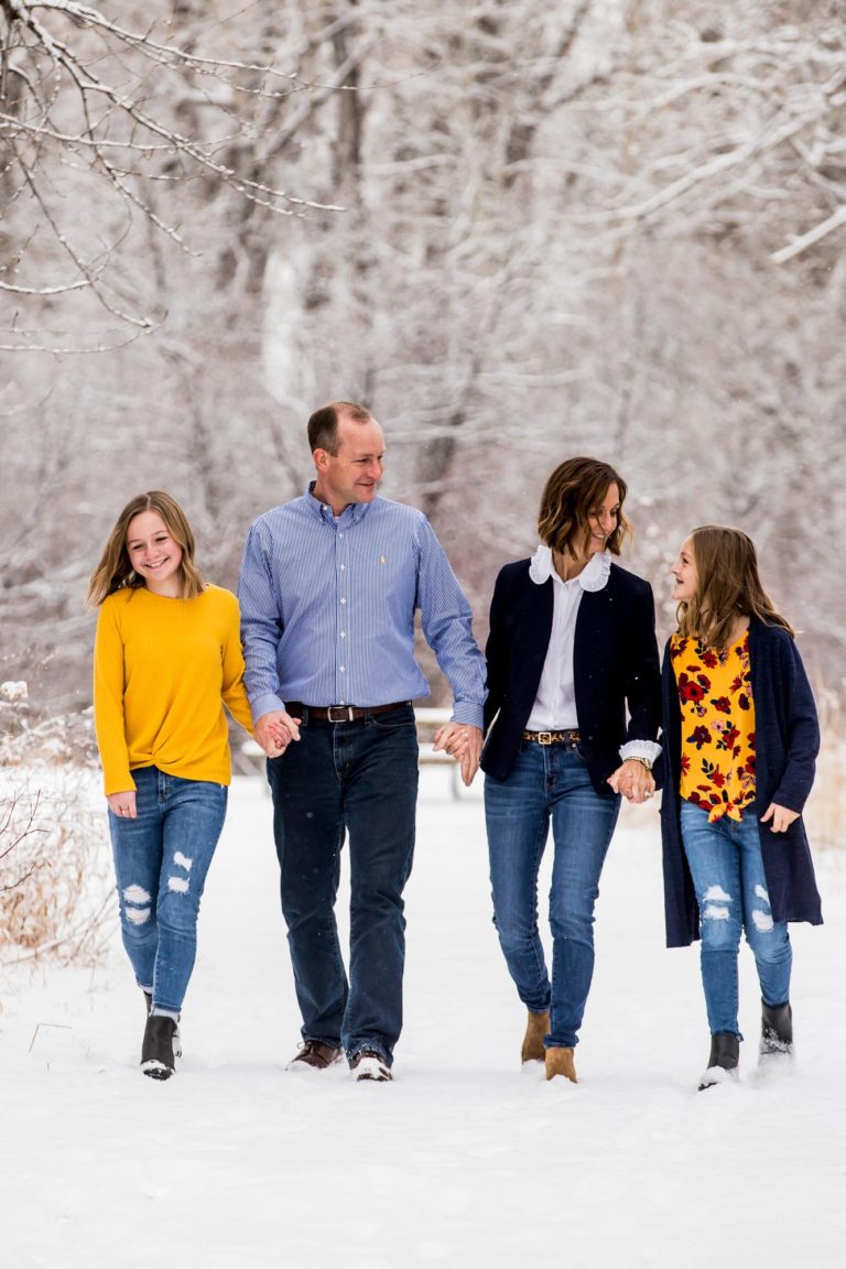 family portrait photography of a mother, father, and teenage daughter walking hand in hand through a field