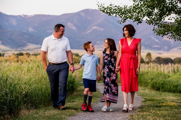 family portrait photography of a mother, father, and teenage daughter walking hand in hand through a field